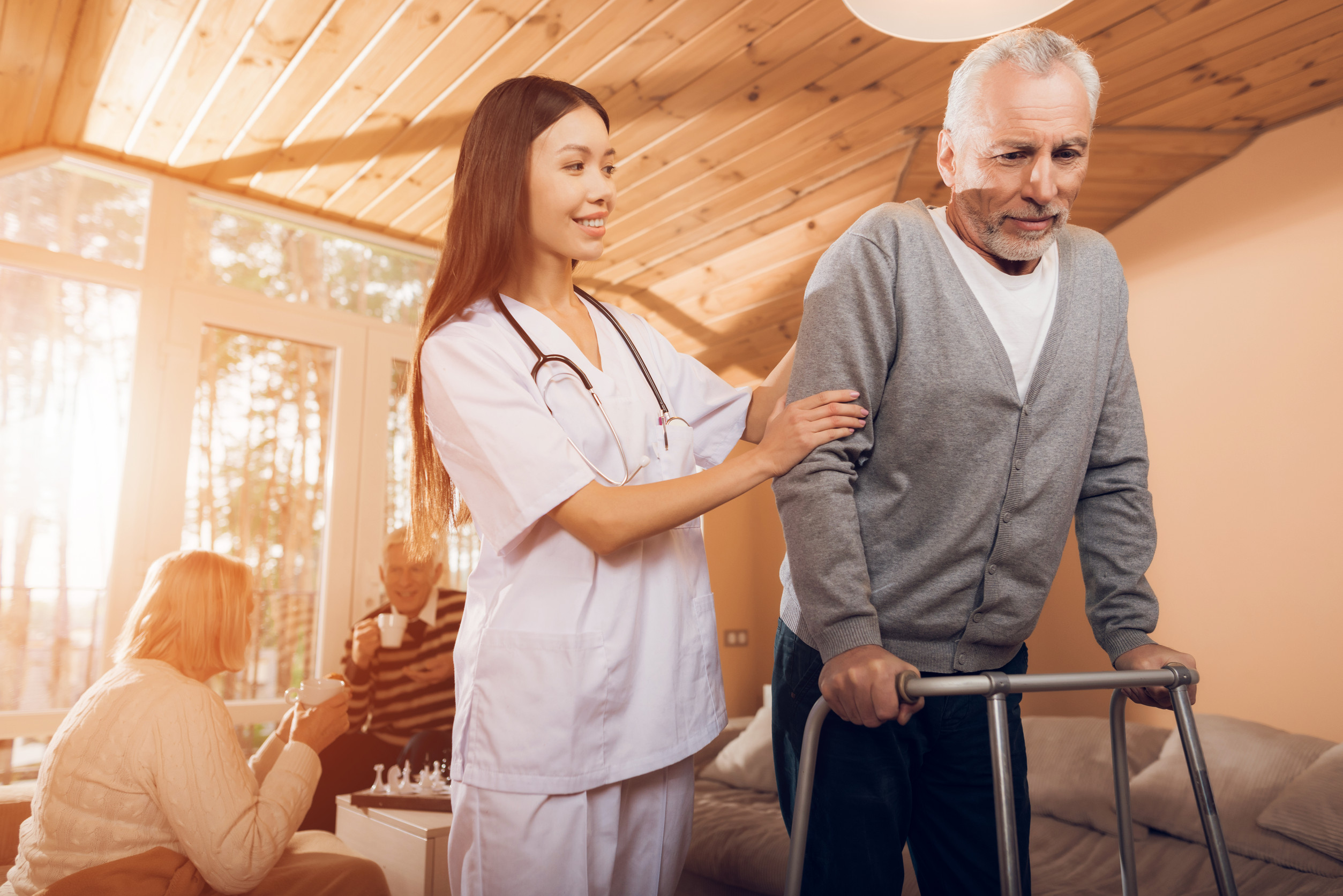 An asian nurse helps a man on an adult walker in a nursing home.